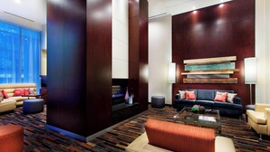 A modern lobby with a large dark wooden column, a fireplace, a sofa, a coffee table, and a patterned carpet.