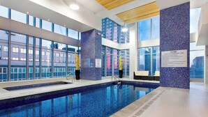 An indoor swimming pool with clear blue water, large windows, and a blue mosaic wall.