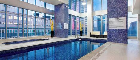 Una piscina interior con agua azul cristalina, ventanas amplias y un muro de mosaico azul.