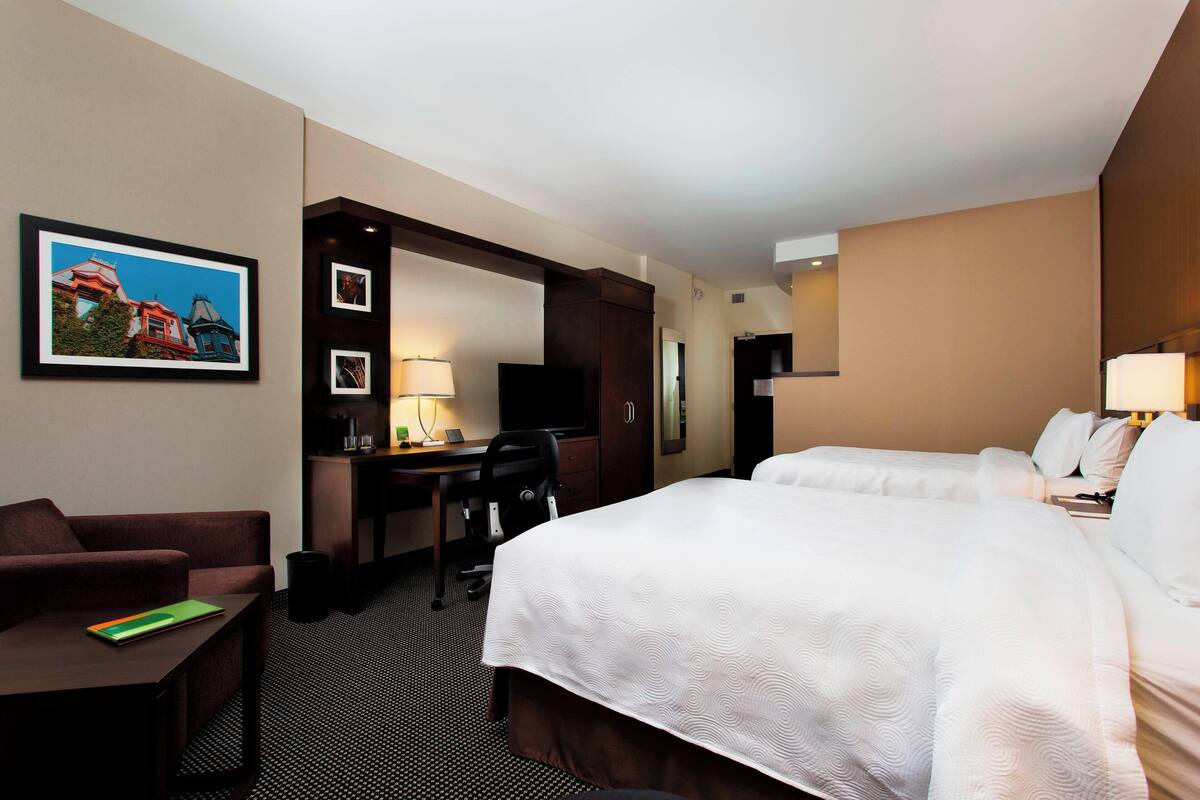 Una habitación de hotel con una cama grande, un escritorio, una silla, un televisor y un cuadro en la pared.