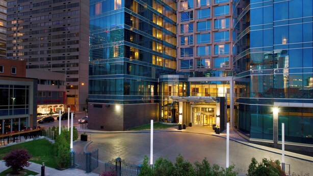 A modern hotel with a glass facade, a landscaped courtyard, and a well-lit entrance.