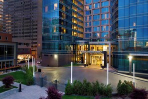 A modern hotel with a glass facade, a landscaped courtyard, and a well-lit entrance.
