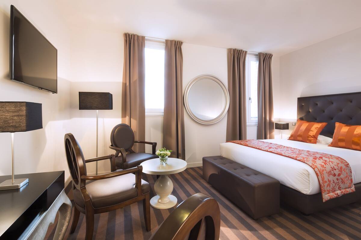 Ein Hotelzimmer mit einem Bett, einem Schreibtisch, einem Sessel, einem runden Tisch und einem Fernseher.
