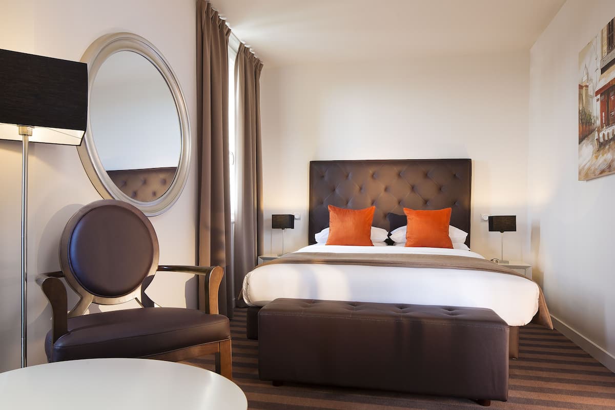 Ein Hotelzimmer mit einem großen Bett, einem runden Spiegel, einem Stuhl und einem kleinen Tisch.