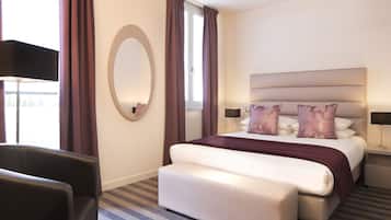 A hotel room with a large bed, a round mirror, a desk, and a chair.