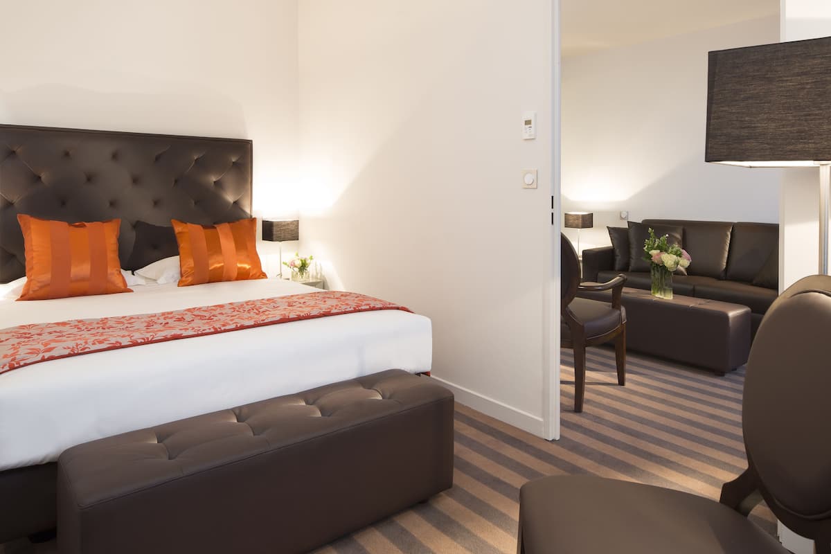 Ein Hotelzimmer mit einem großen Bett, einem Sofa, einem Sessel und einem an der Wand befestigten Fernseher.