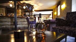 Un coin bar avec une bouteille de cognac, deux verres et une bougie sur une table.