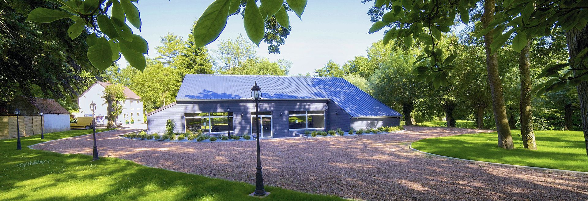 Un bâtiment moderne doté d’un toit en pente, entouré d’une pelouse bien entretenue et d’arbres.