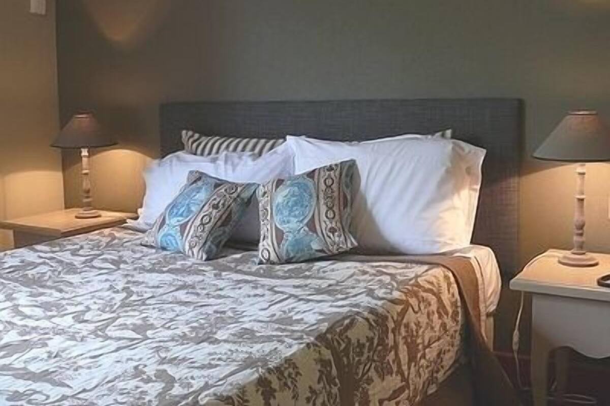 A neatly made bed with patterned bedding, two bedside lamps, and a plain wall.