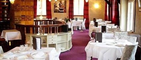 Un restaurante con pared de ladrillo, mesas blancas y cortinas rojas.