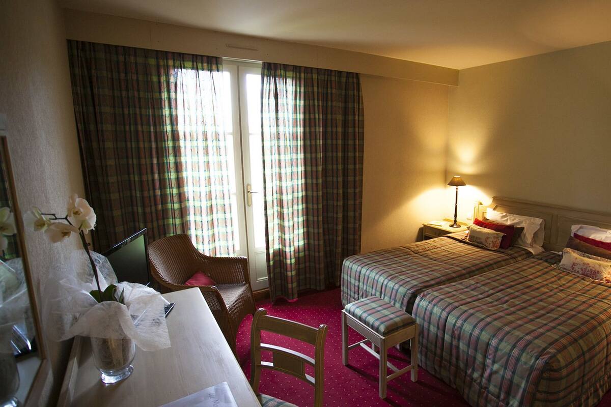 A hotel room with two beds, a desk, a chair, and a window with curtains.