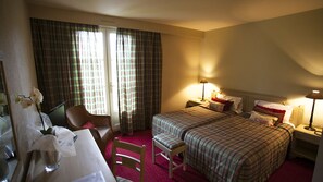 Une chambre d’hôtel avec deux lits, un bureau, une chaise et une fenêtre avec des rideaux.
