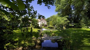 Un jardin paisible avec un étang, un pont en bois et un bâtiment historique doté d’une roue à eau.