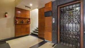 A reception area with a wooden reception desk, a fire extinguisher, a television, and a security gate. - Hotel Imperial Classic (Hyderabad)