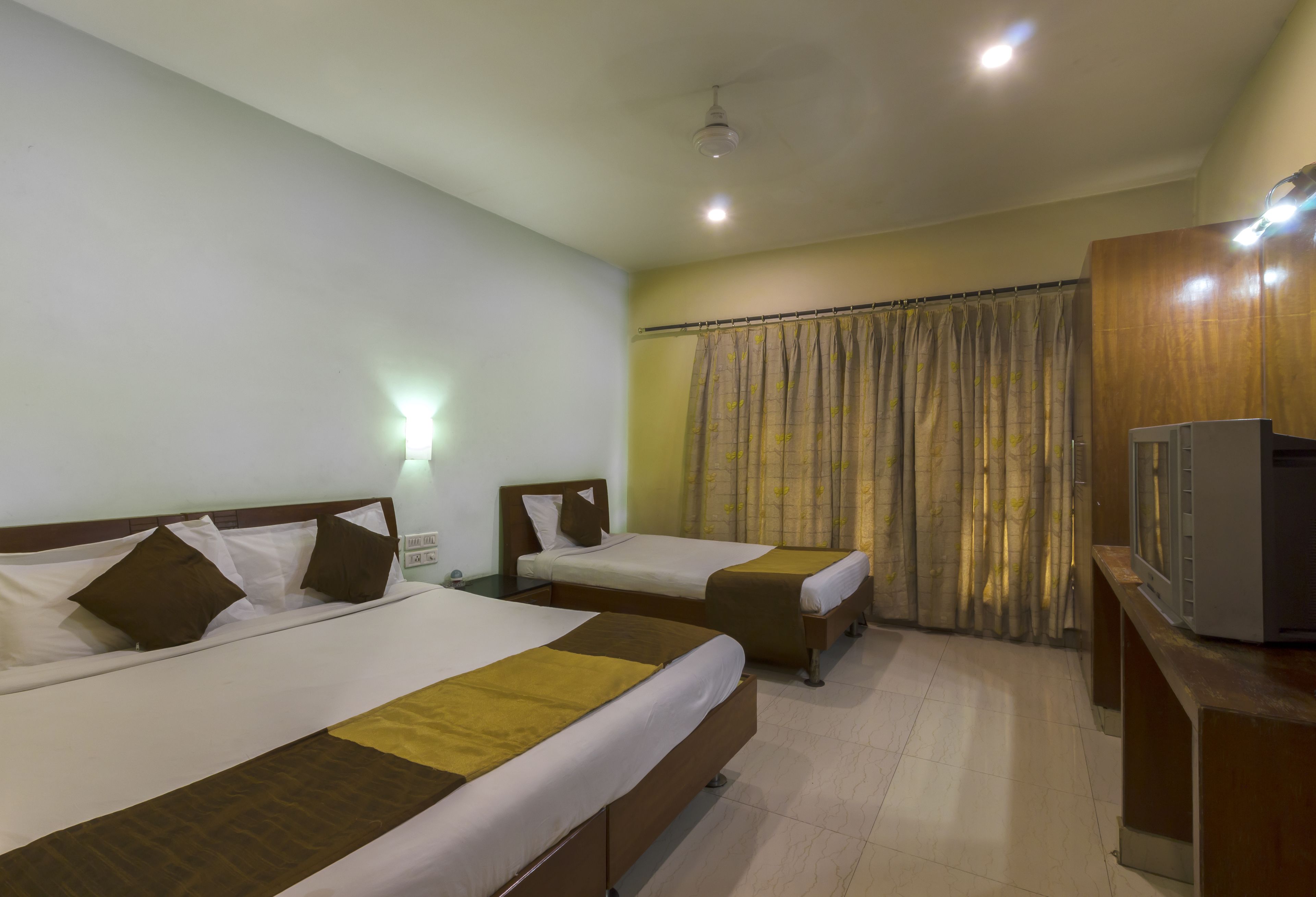A hotel room with two beds, a TV, and a curtain.