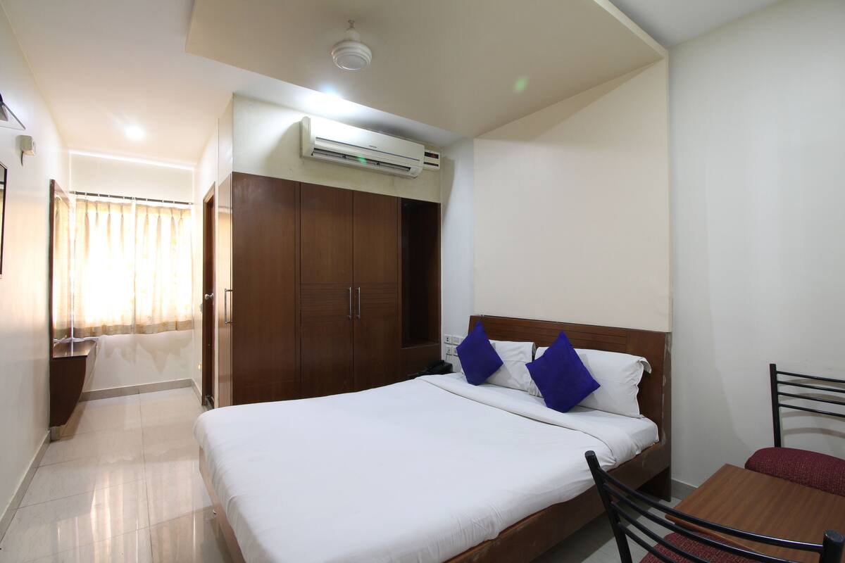 A hotel room with a bed, a wooden wardrobe, a table, and a chair.