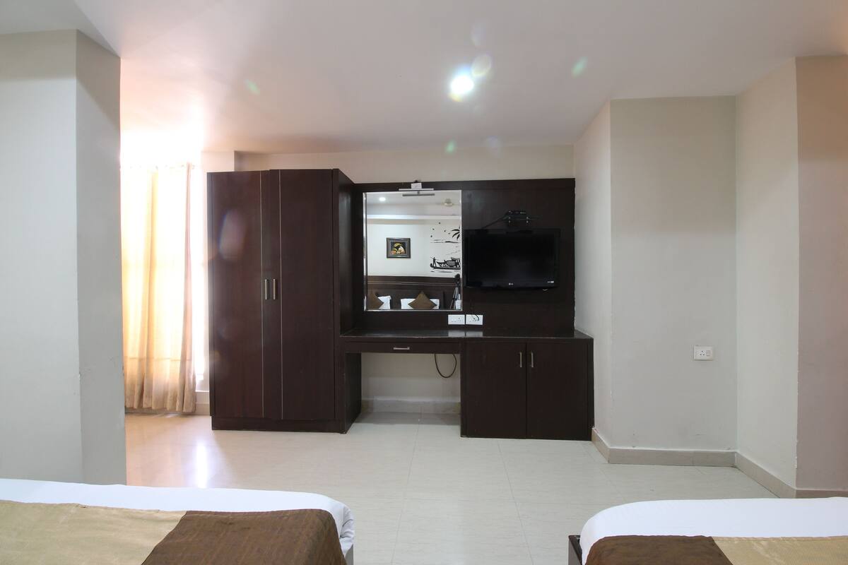 A hotel room with two beds, a desk with a flat-screen TV, a mirror, and a wardrobe.