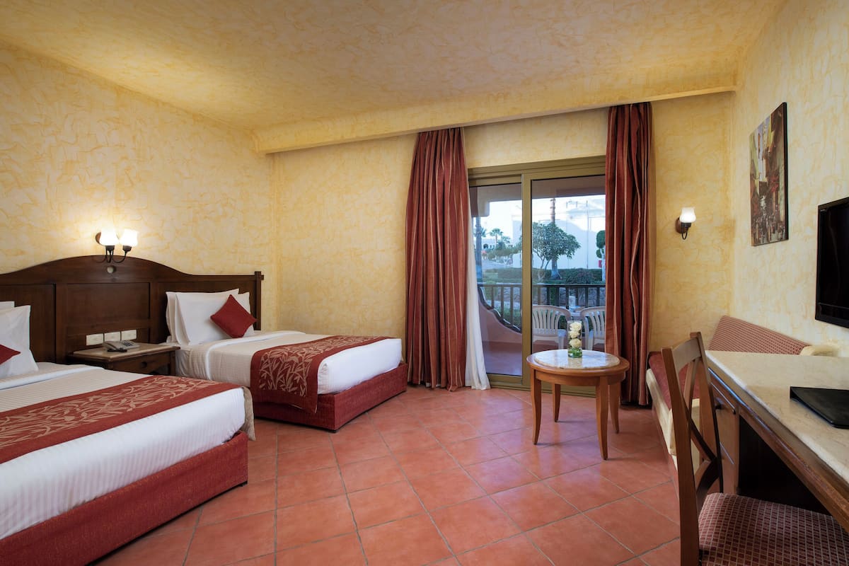 A hotel room with two beds, a desk, a chair, a TV, and a balcony with curtains.