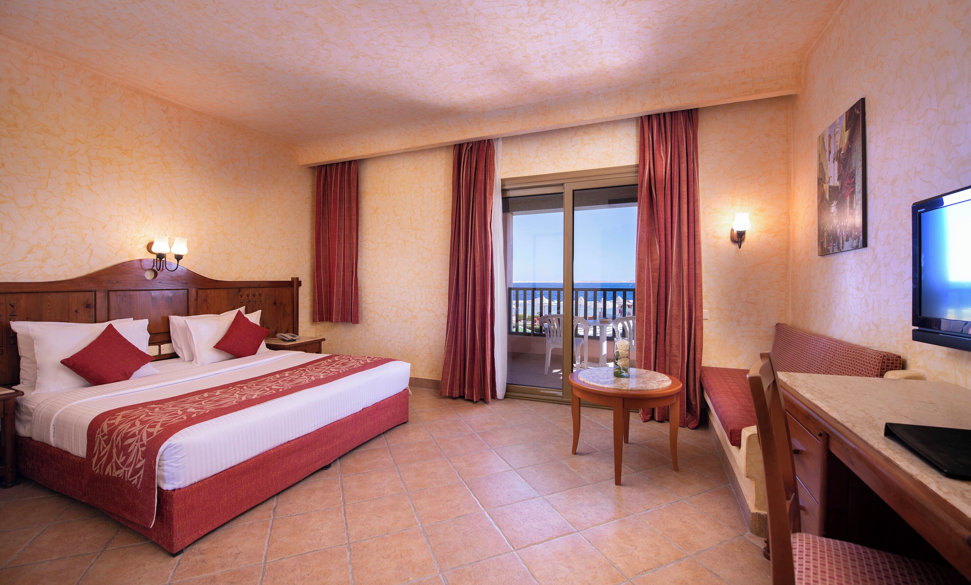 Une chambre d’hôtel avec un lit, un bureau, une chaise, une télévision et un balcon avec des rideaux.