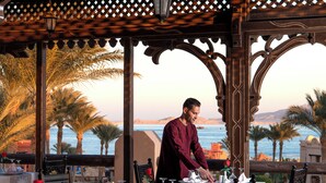 A dining area with tables set for two, overlooking a coastal view with palm trees and a body of water. - Charmillion Sea Life Resort (Sharm El Sheikh)