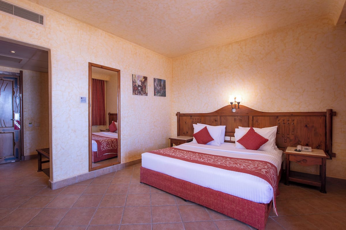 A hotel room with a large bed, a wooden headboard, a nightstand, a bedside table, a mirror, and a door leading to another room.