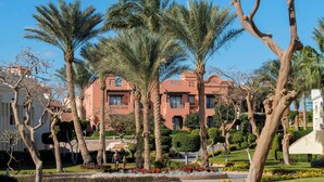 A landscaped garden with palm trees, a building with balconies, and a clear blue sky. - Charmillion Sea Life Resort (Sharm El Sheikh)
