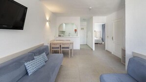 A modern, well-lit room with a sofa, a television, a small dining area, and a bathroom visible in the background.