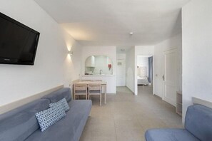 A modern, well-lit room with a sofa, a television, a small dining area, and a bathroom visible in the background.