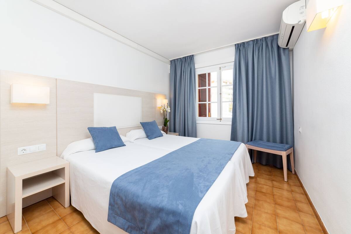 Una habitación de hotel con cama, mesita de noche y ventana con cortinas.