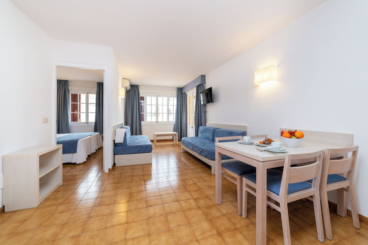 Una habitación moderna y luminosa con una mesa de comedor, sillas, un sofá y un televisor montado en la pared.