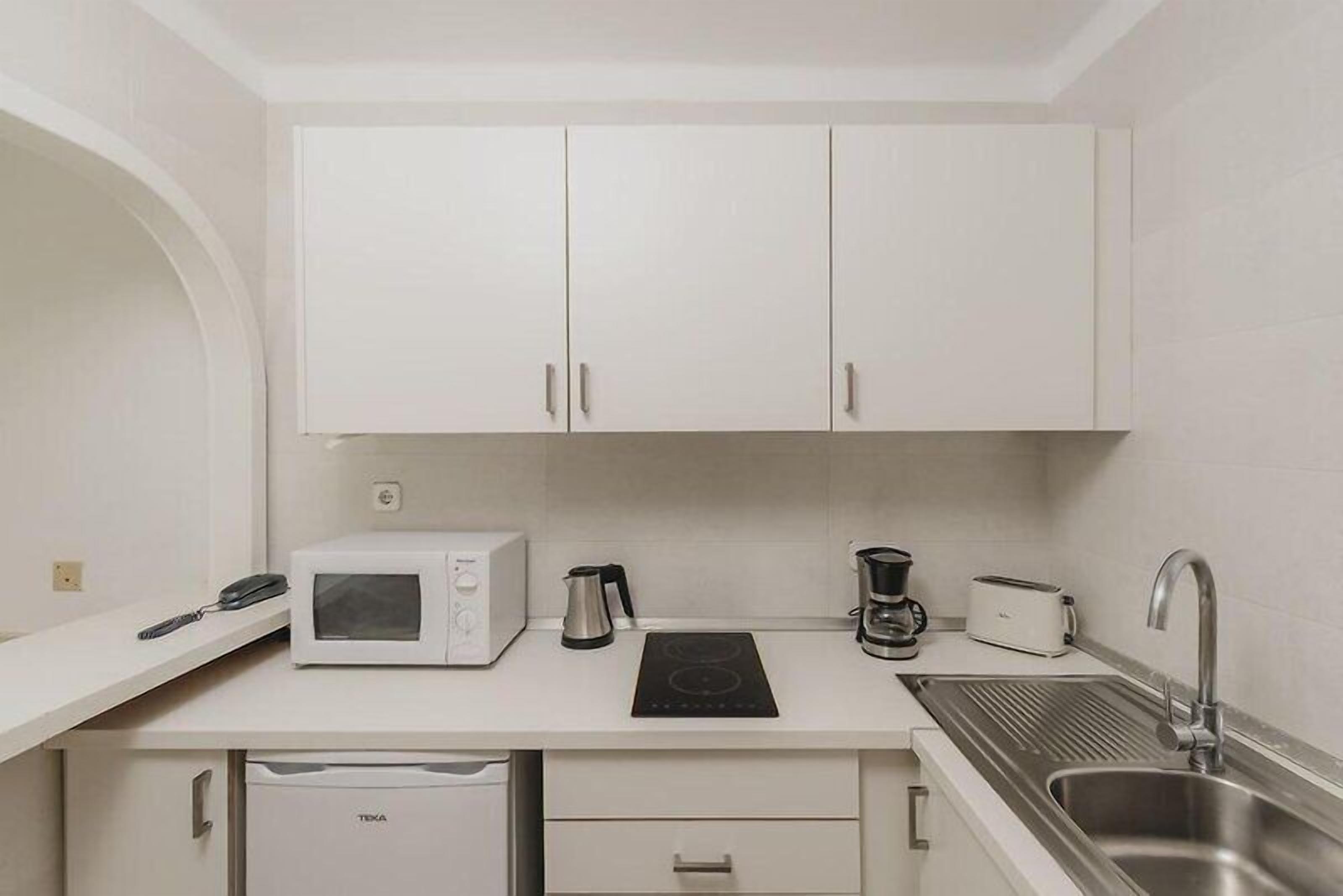 A compact kitchenette with a microwave, coffee maker, toaster, and sink.