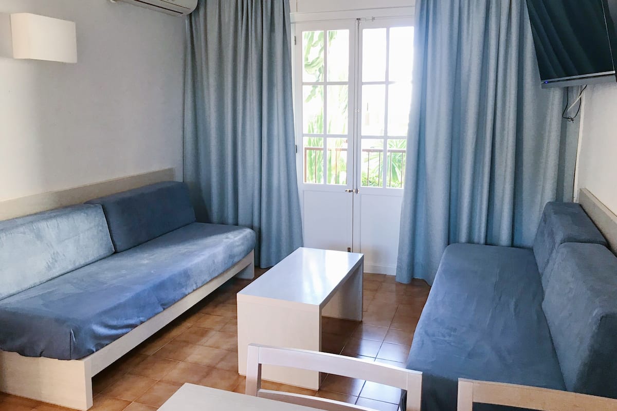 Una habitación con un sofá, una mesita blanca y un televisor montado en la pared.