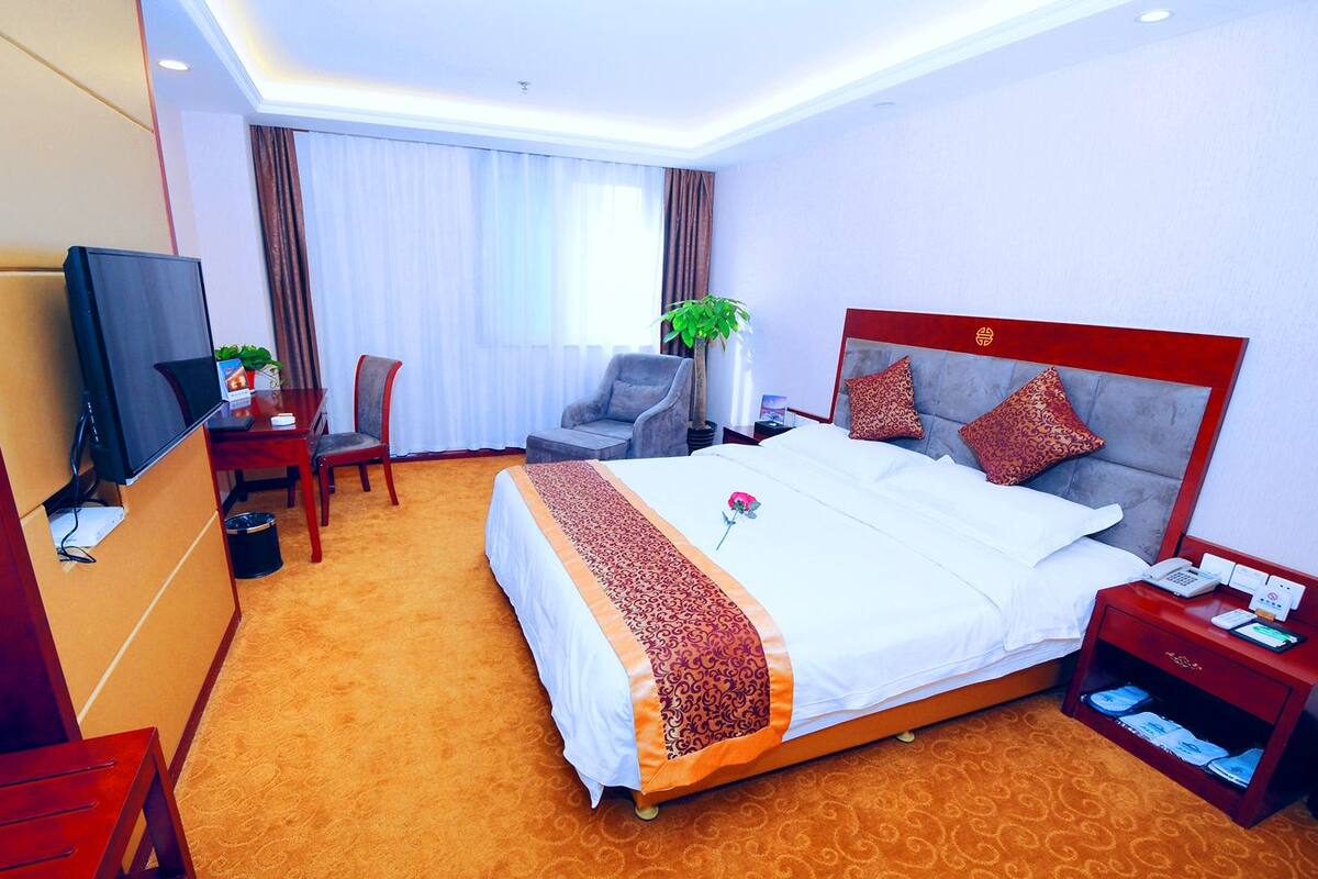 A hotel room with a large bed, a desk with a chair, a TV, and a plant.