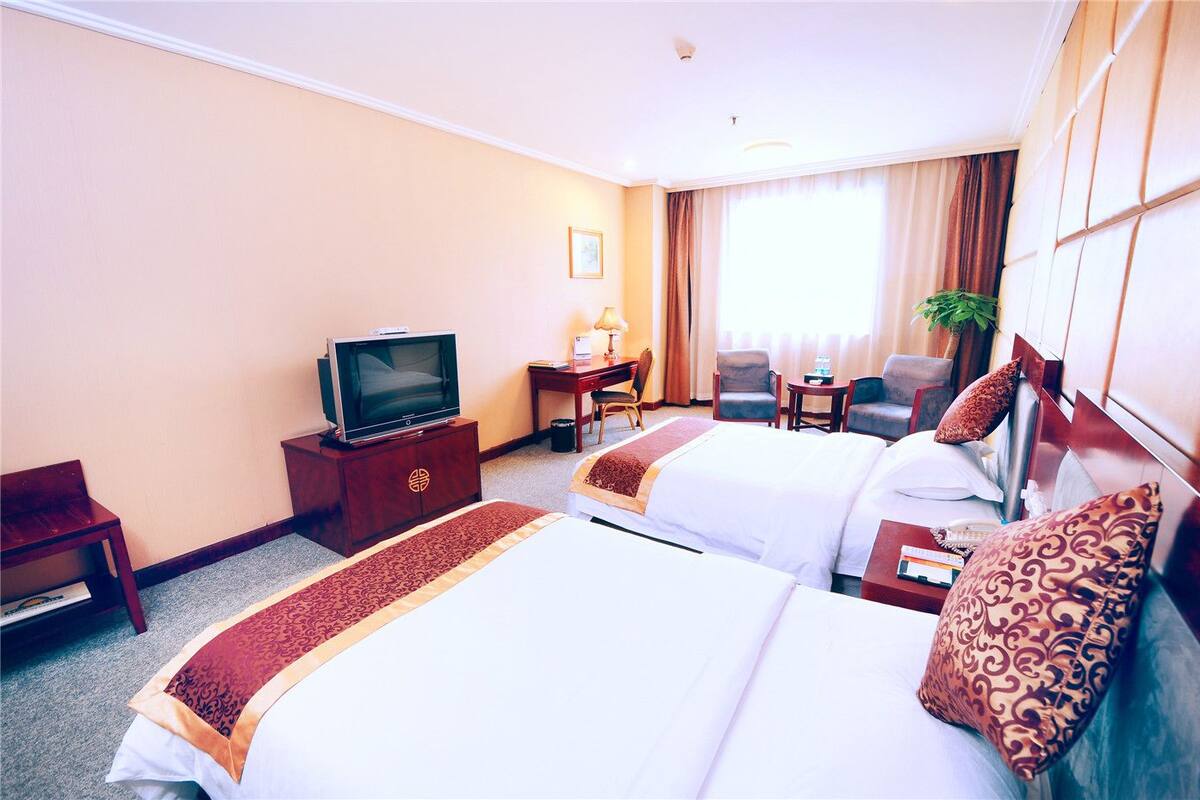 A hotel room with two beds, a desk, a chair, a television, and a window with curtains.