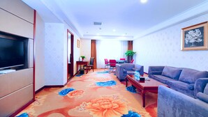 A hotel room with a TV, a sofa, a coffee table, a dining area with chairs, and a carpet with floral patterns. - Days Inn By Wyndham City Centre Xian (Xi'an)