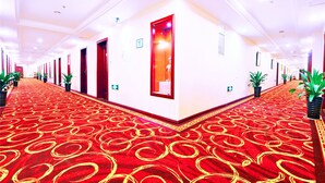 A hotel corridor with red carpet, multiple doors, potted plants, and a large mirror on the wall. - Days Inn By Wyndham City Centre Xian (Xi'an)