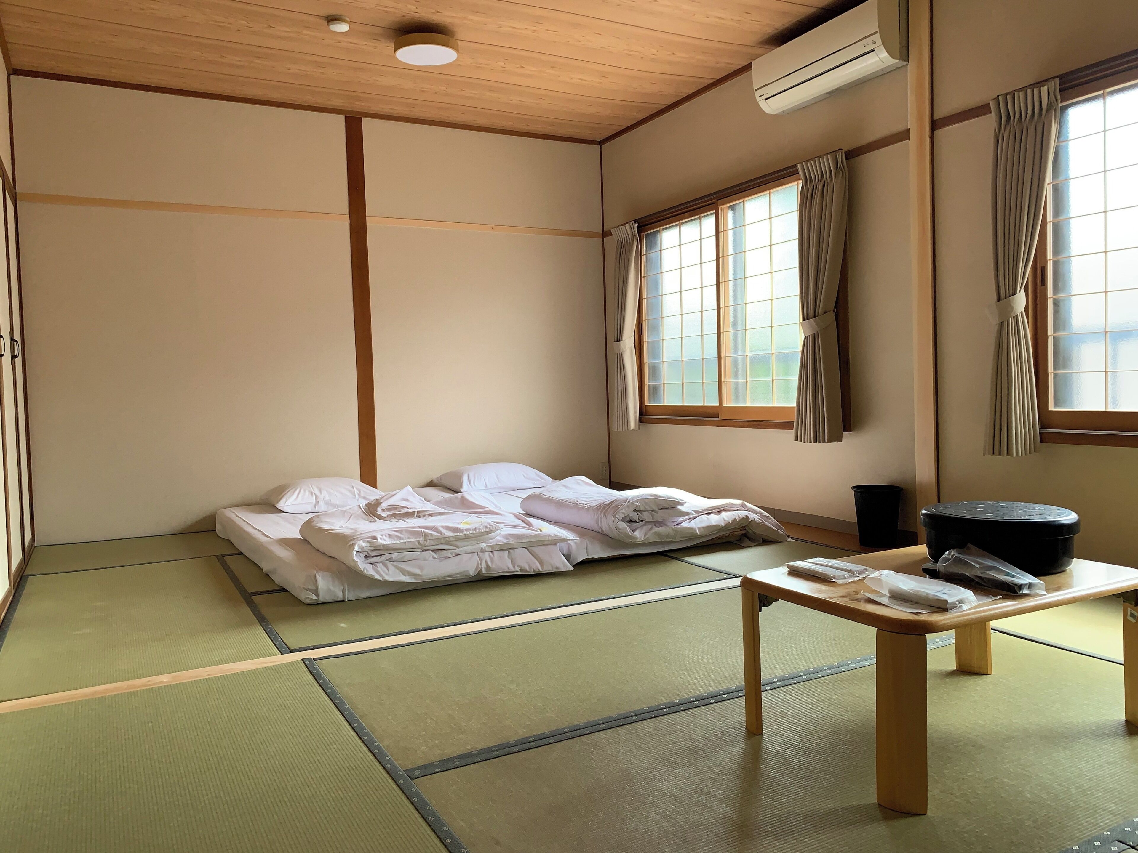 Une pièce de style japonais traditionnel, avec un sol recouvert de tatamis, un futon servant de lit, une table en bois et une fenêtre avec des rideaux.