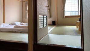 A traditional Japanese room with tatami flooring, a futon bed, sliding shoji doors, and a window with curtains. - Minshuku Kuwataniya (Takayama)