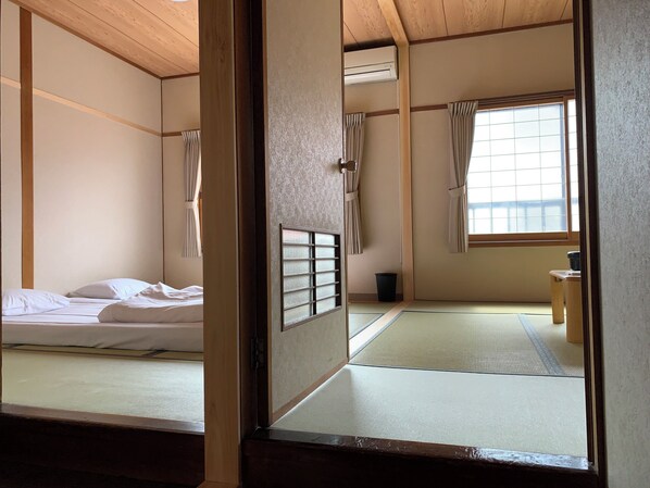 A traditional Japanese room with tatami flooring, a futon bed, sliding shoji doors, and a window with curtains. - Minshuku Kuwataniya (Takayama)