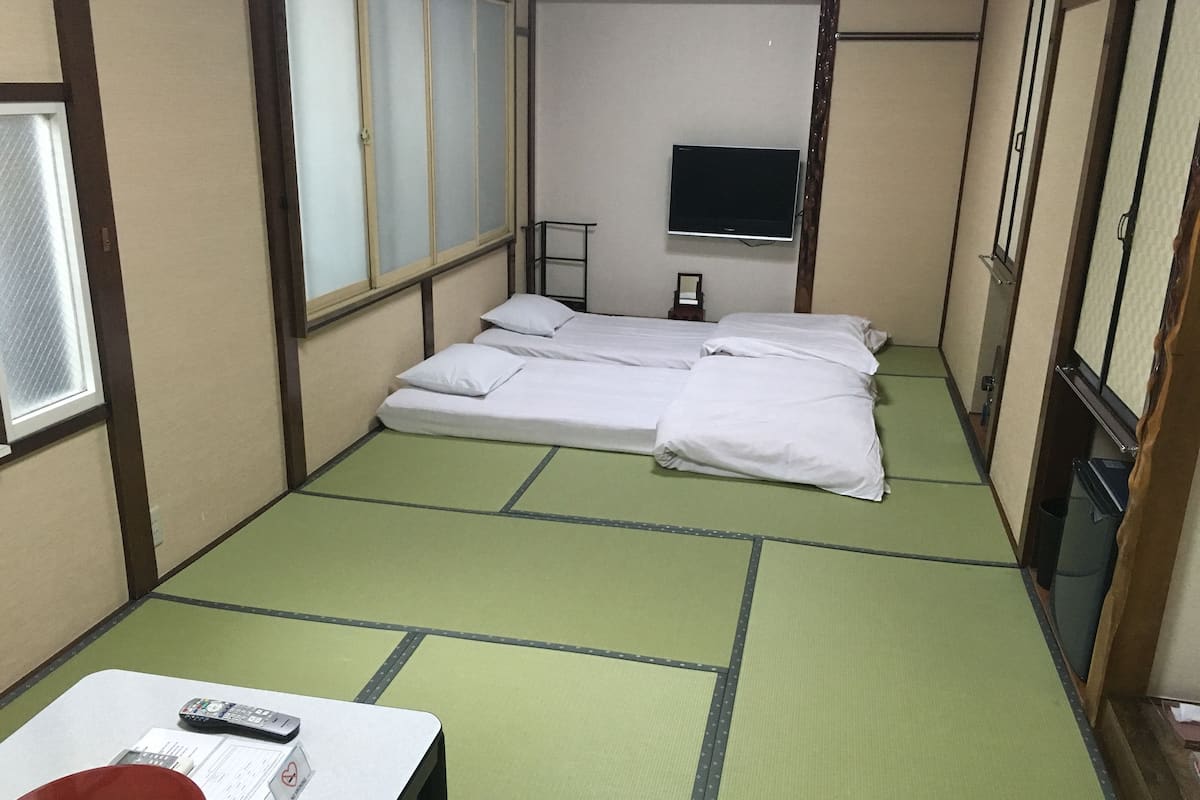 A room with a bed, a TV, a table with a remote, and a window.