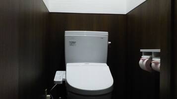 Casa de banho compacta e moderna, com sanita, uma pequena janela sobre a sanita e um rolo de papel higiénico fixado na parede.