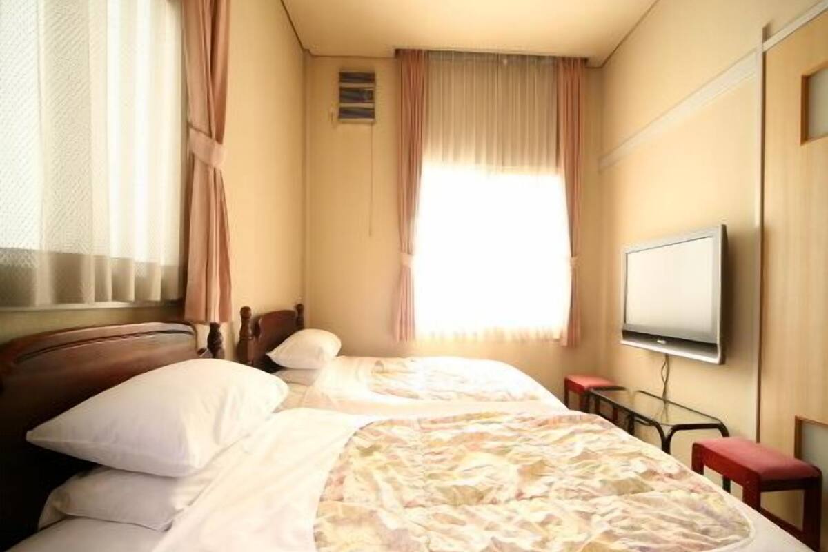 A hotel room with two beds, a television, and a window with curtains.