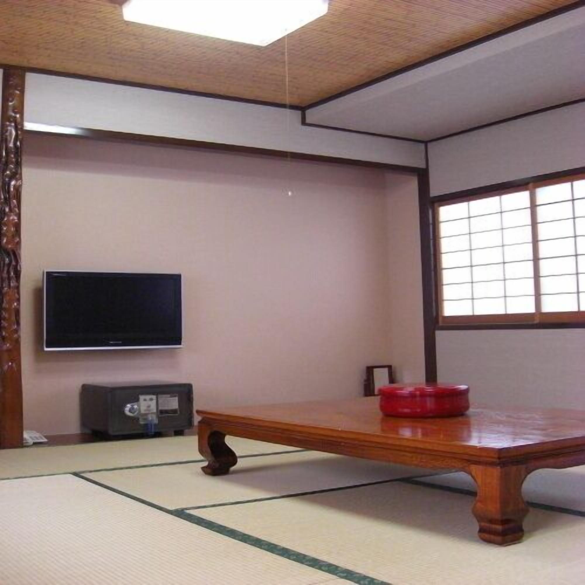 Une pièce de style japonais traditionnel, avec un sol recouvert de tatamis, une petite table en bois, un téléviseur et une fenêtre à carreaux.