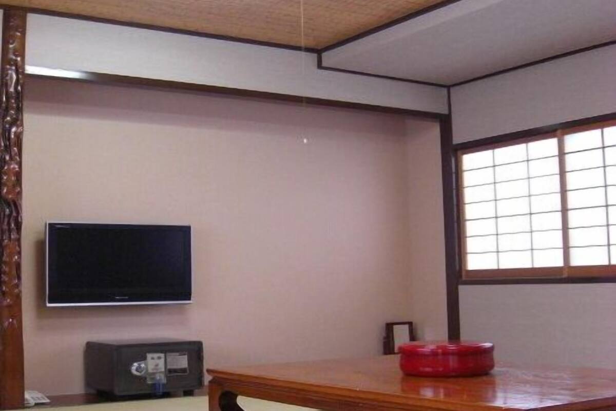 A traditional Japanese room with tatami flooring, a low wooden table, a television, and a window with a grid pattern.