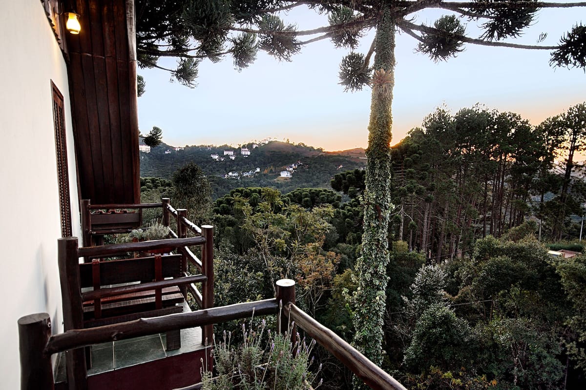 Eine Holztreppe führt zu einem Balkon mit Blick auf eine bewaldete Landschaft und entfernte Häuser.