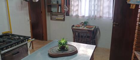 Una cucina con un fornello, pentole, un tavolo da pranzo con sedie e una finestra con tende.