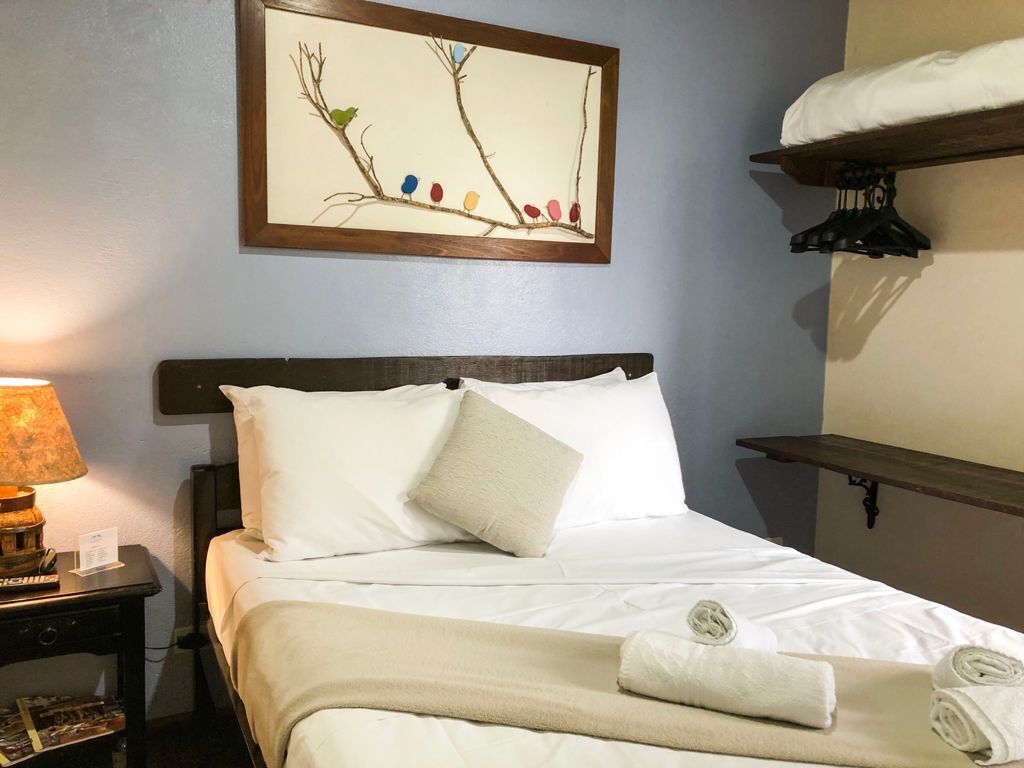 A neatly made bed with white linens and a beige throw blanket, a bedside lamp, and a framed artwork above the bed.