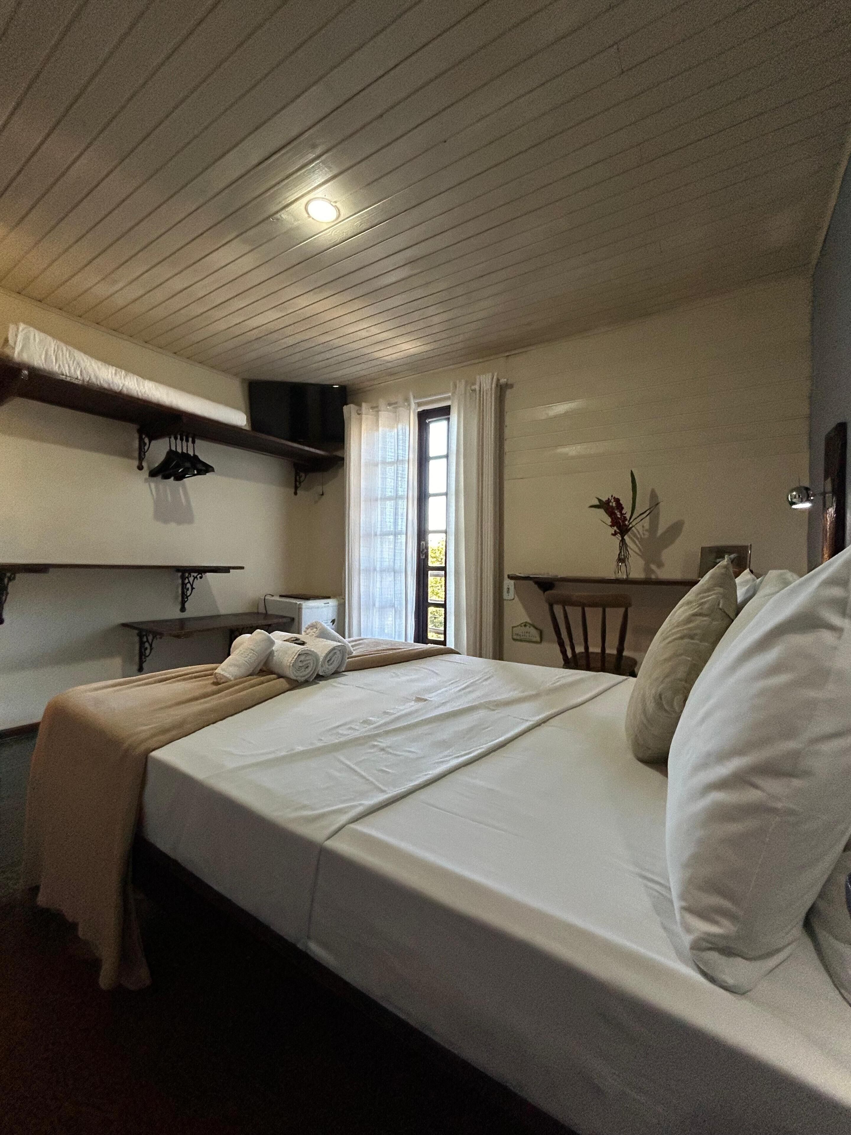 A hotel room with a large bed, a small table, a chair, and a window with curtains.