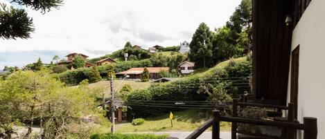 Vista desde un balcón sobre una colina con varias casas, una valla de madera y cielo despejado.