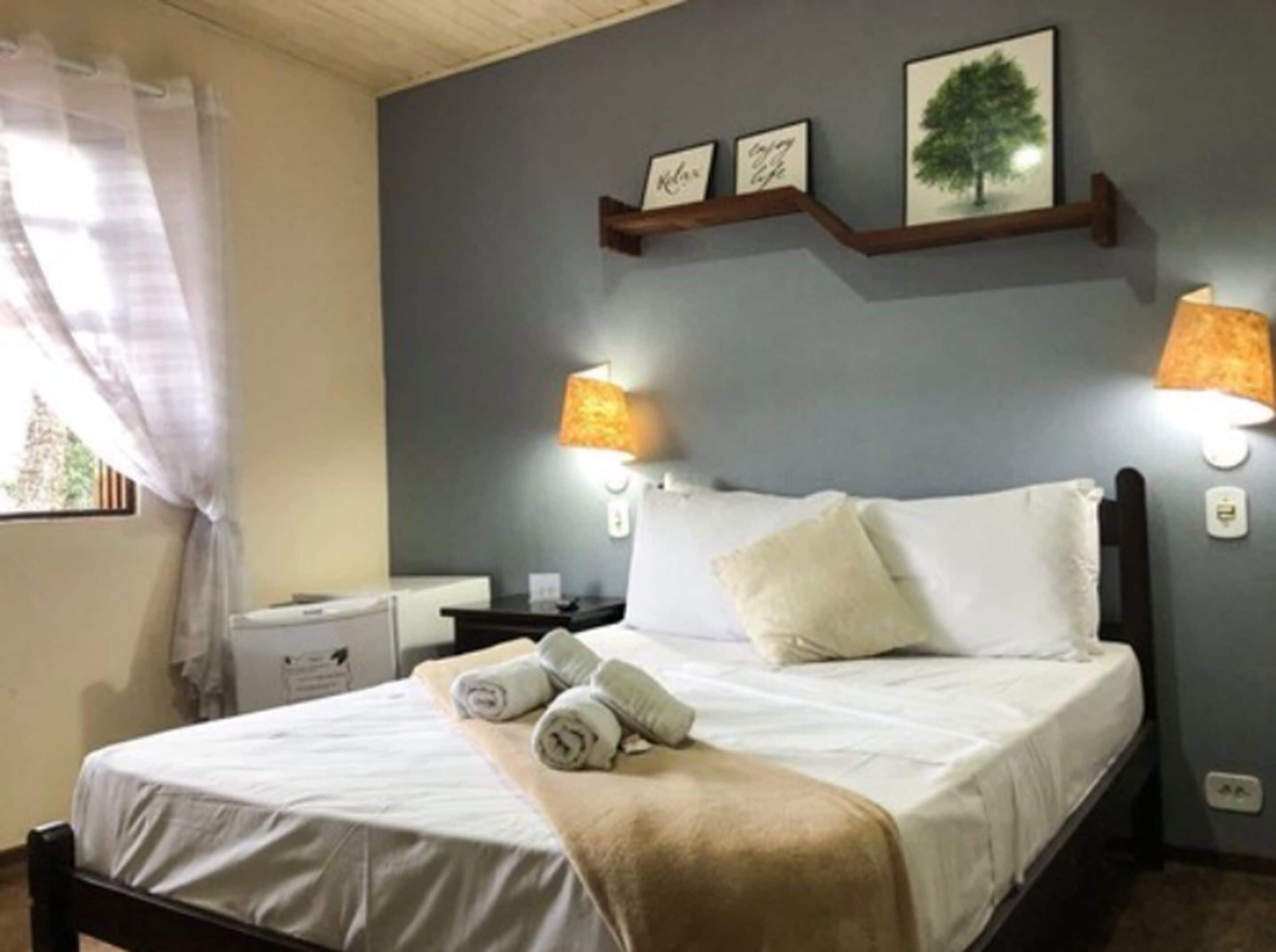 A neatly made bed with white linens and a beige throw blanket, a nightstand with a lamp, and wall-mounted picture frames.